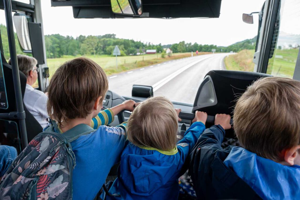 Drei Kinder sitzen im Bus und schauen vorne raus.