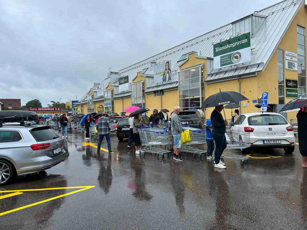 Menschen mit Einkaufswagen und Regenschirmen stehen Schlange vor dem Gekås-Supermarkt.