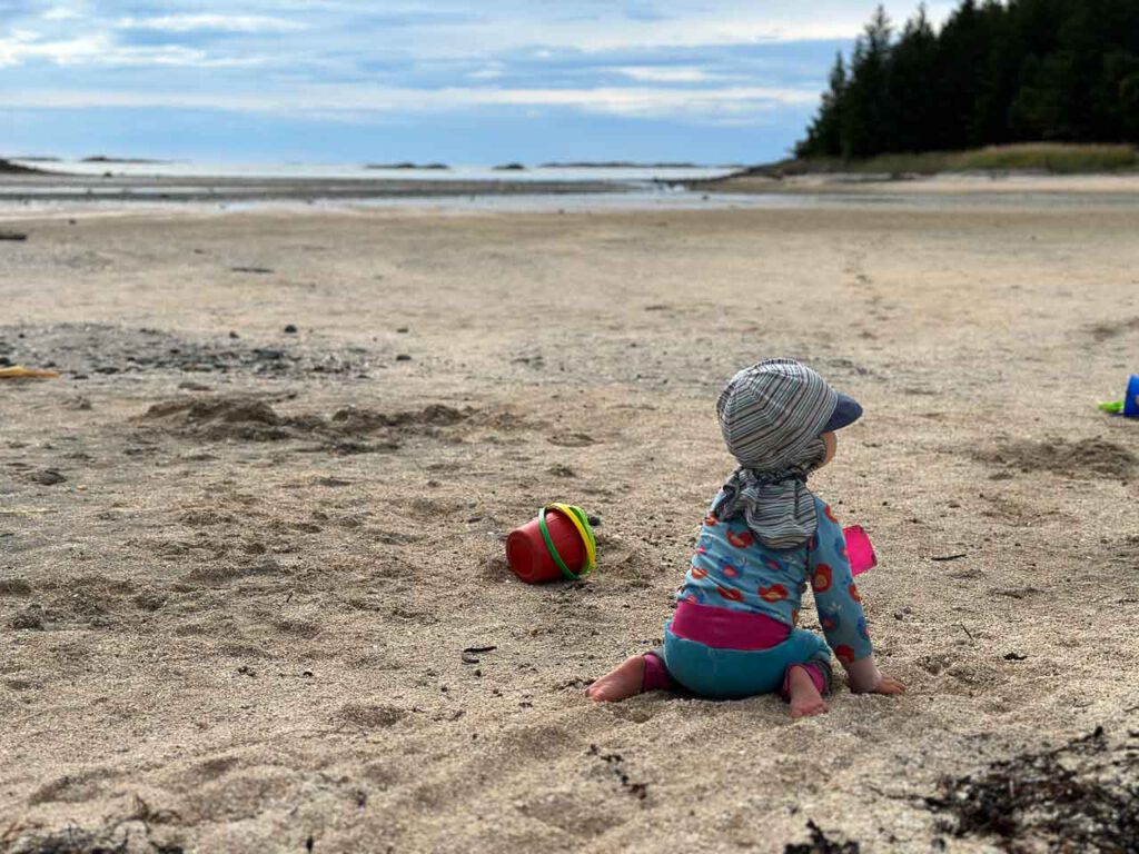Kleinkind sitzt am Strand im Sand.