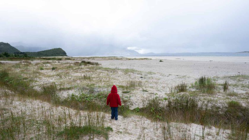 Ein Kind steht mit dem Rücken zum Betrachter und schaut auf einen sehr großen Sandstrand.