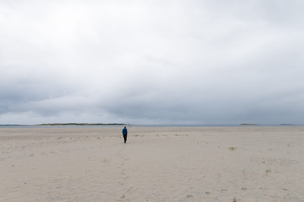 Ein Mann mit Babytrage läuft in der Ferne über einen breiten Strand.