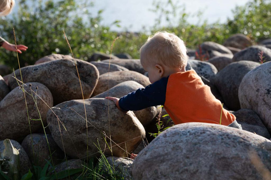 Ein kleines Krabbelkind spielt auf großen Flusssteinen.