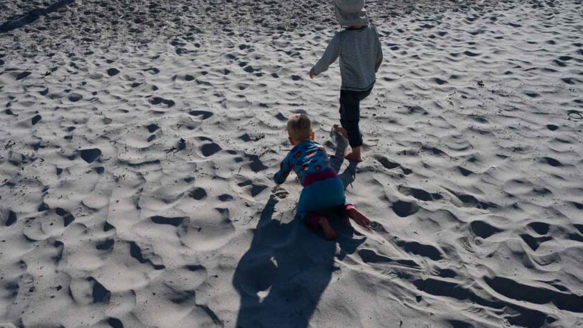 Ein kleines Kind und ein Baby am Strand.