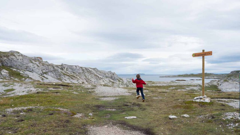 Ein Kind rennt auf einem Wanderweg, daneben ein Wegweiser.